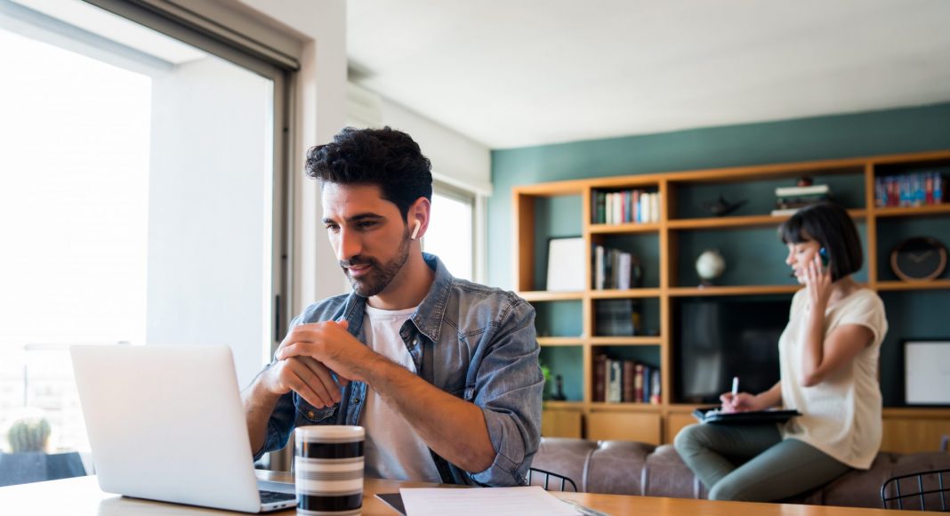 portrait of young man working with a laptop from home while woman talking on phone