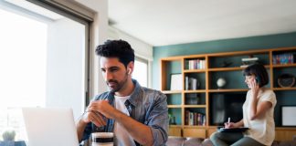 portrait of young man working with a laptop from home while woman talking on phone