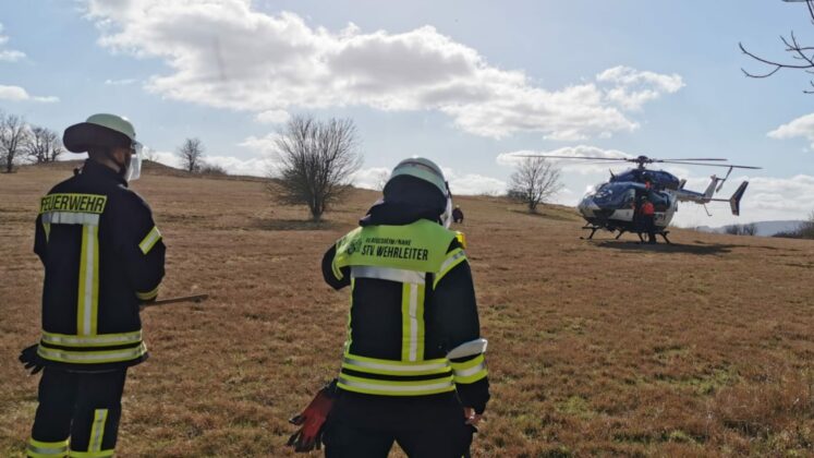 Feuerwehrleute vor einem Polizeihubschrauber, Symbolbild